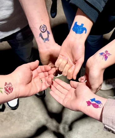 Hier sieht man Arme auf denen mit Hilfe der Glitzerbar Glitzertattoos angebracht wurden. Unterschiedliche Motive wie verliebte J´Katzen, Elefant, Rose, Schmetterling und Pinguin schmücken die Damen Handgelenke. Gesichtsbemalung für Corporate Events