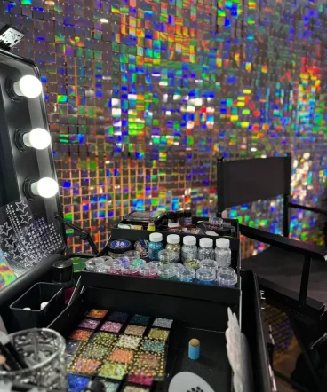 Professionelle Glitzer-Schminkstation mit Make-up-Spiegel, buntem Glitzer, Strasssteinen und holografischer Paillettenwand.