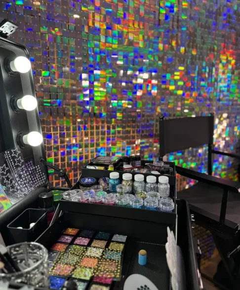 Professionelle Glitzer-Schminkstation mit Make-up-Spiegel, buntem Glitzer, Strasssteinen und holografischer Paillettenwand.