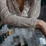 Hier sieht man den Oberkörper einer Frau in einem silbernen Glitzerkleid. Sie lehnt auf einer großen Discokugel. Corporate Events Firmenfeier