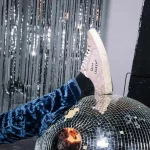 Hier sieht man einen Lametta Vorhang im Hintergrund. Vorne ist eine Discokugel zu sehen auf der ein Bein abgelegt ist. Teambuilding Frankfurt Corporate Events