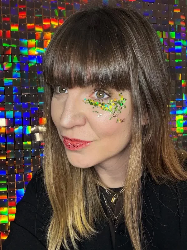 Glitzer-Makeup in Gold und Grün mit Schmetterlingsmotiven auf einer Frau vor einem schimmernden Hintergrund